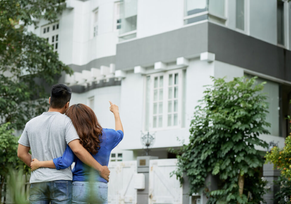 Dreamy young couple looking at big house, view from the back