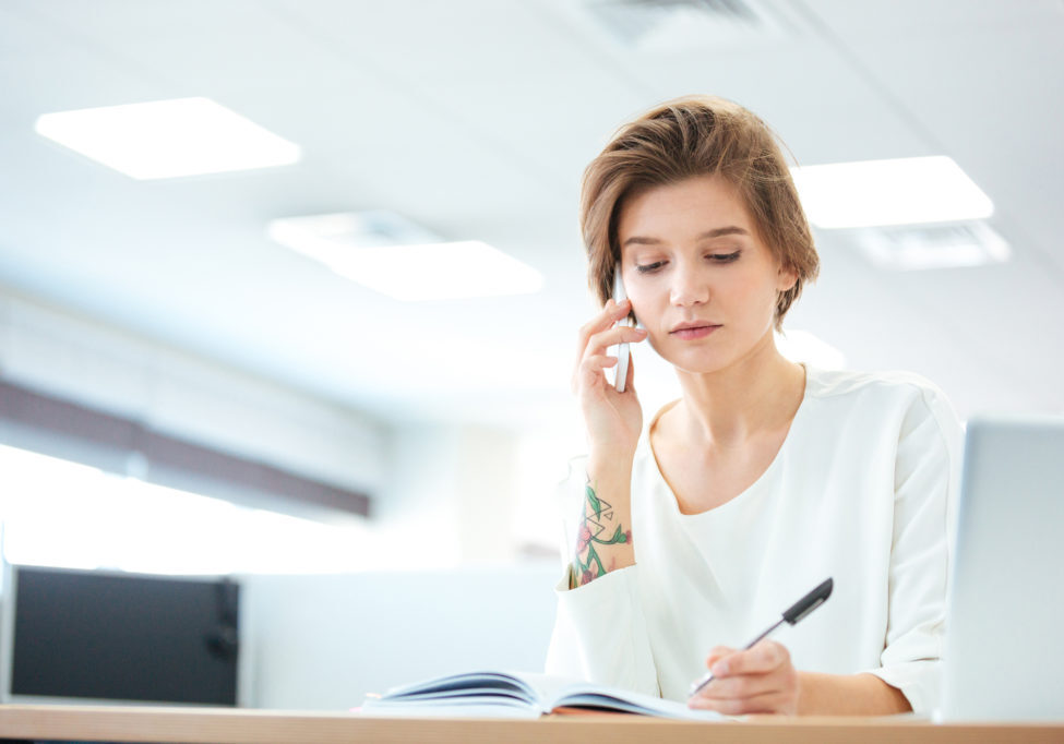 Businesswoman talking on the phone in office and writing notes